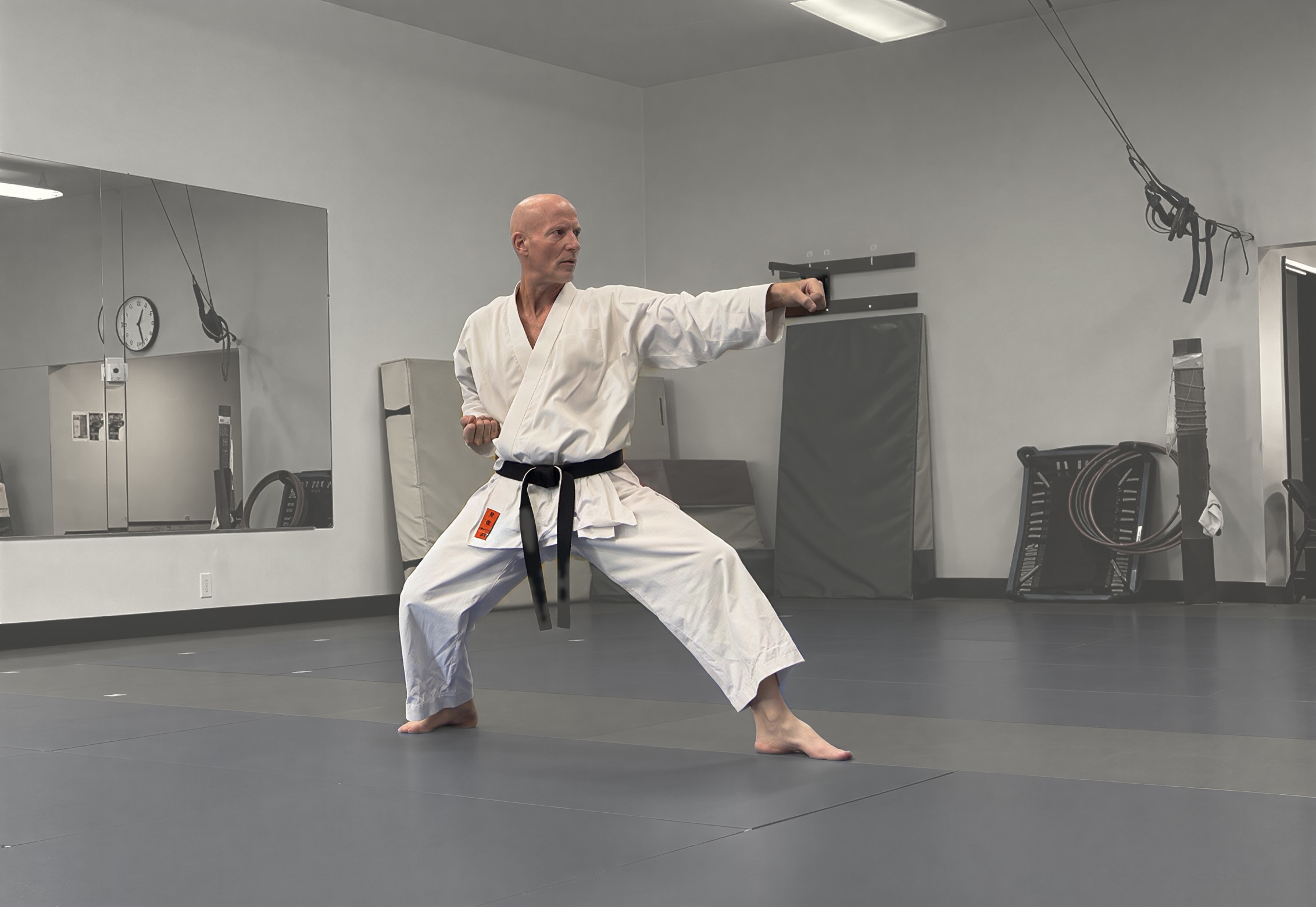 Eran Shine in a white karate gi and black belt, in a low stance, throwing a punch in the dojo.